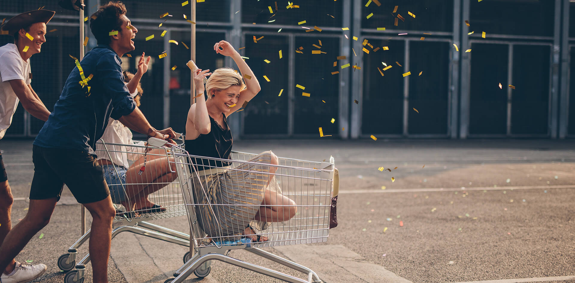 Glückliche Kundinnen und Kunden sitzen in einem Einkaufswagen.